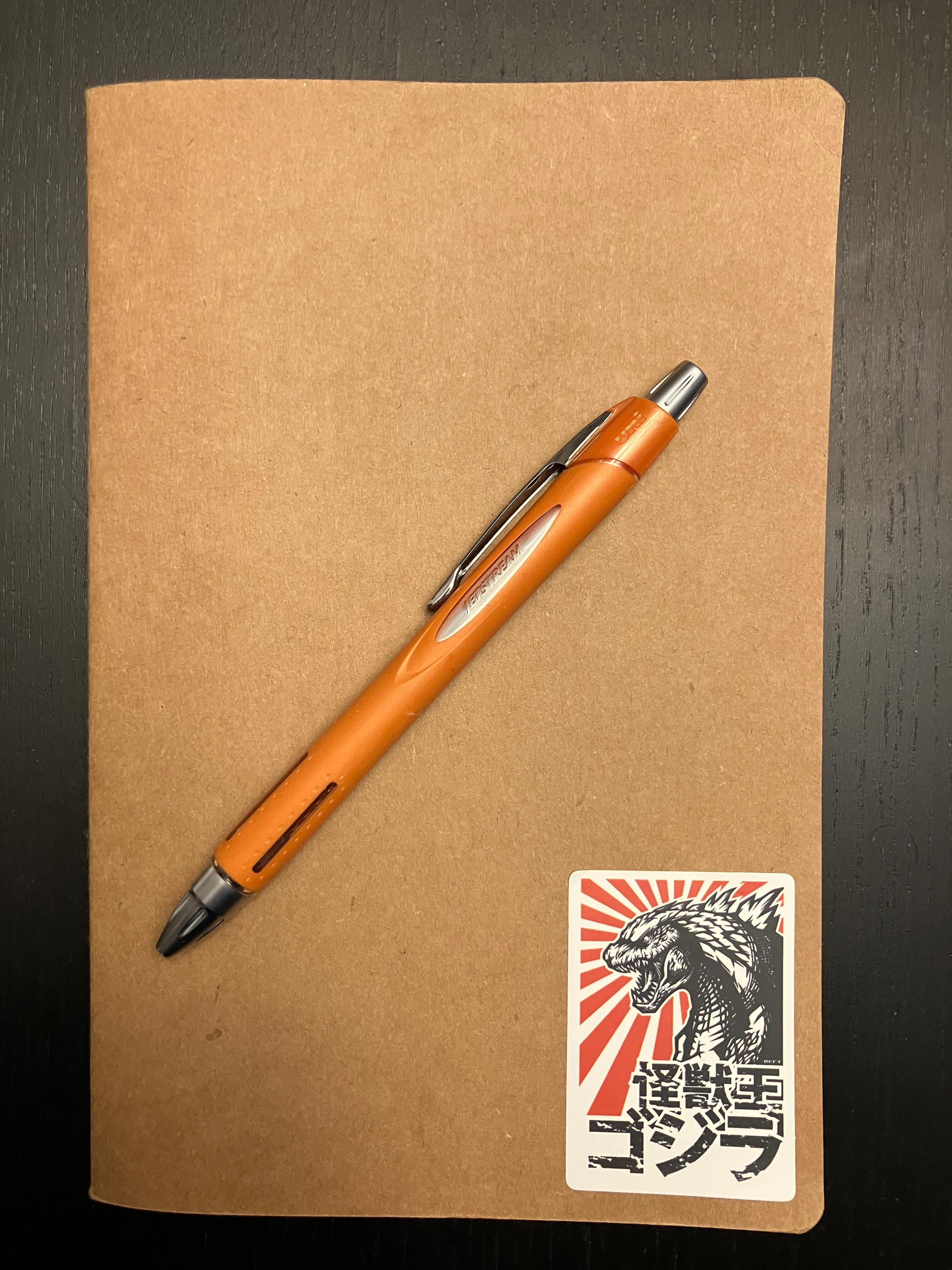 A simple, A5 notebook with a plain cardboard cover with a Godzilla sticker on the bottom right corner.